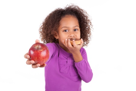 Little African Asian girl eating a chocolate cake and holding an apple, isolated on white backgroundの写真素材