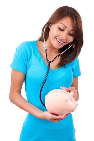 Young happy beautiful asian woman using stethoscope on her piggy bank, isolated on white background - Asian peopleの写真素材