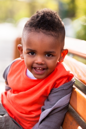 Outdoor portrait of a cute young  little black boy seated on a bench - African peopleの写真素材