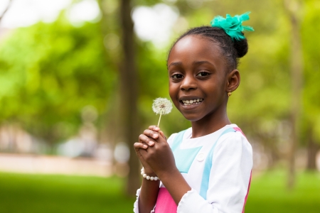 Outdoor portrait of a cute young black girl holding a dandelion flower - African peopleの写真素材