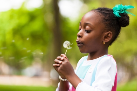 Outdoor portrait of a cute young black girl blowing a dandelion flower - African peopleの写真素材