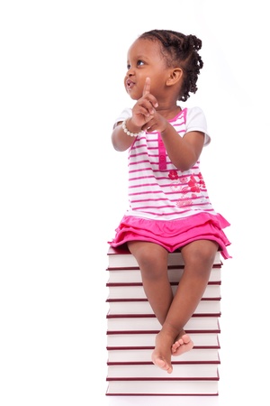 Cute black african american little girl seated in a stack of books, isolated on white background - African people - Childrenの写真素材