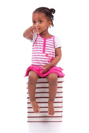 Cute black african american little girl seated in a stack of books, isolated on white background - African people - Childrenの写真素材