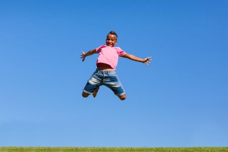 Outdoor portrait of a cute teenage black boy jumping over a blue sky - African peopleの写真素材