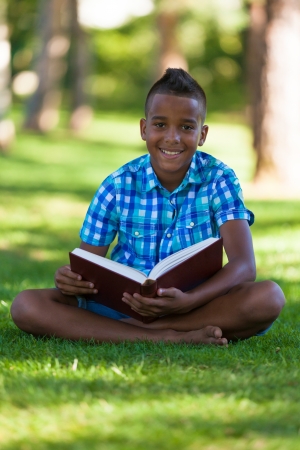 Outdoor portrait of student black boy reading a book - African peopleの写真素材