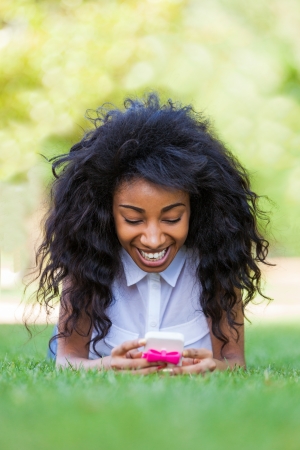 Smiling teenage black girl using a phone, lying down on the grass - African peopleの写真素材