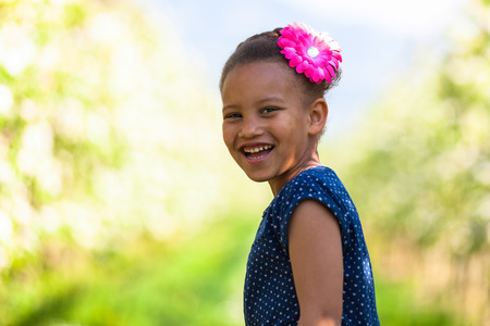 Outdoor portrait of a cute young black girl  lying down on the grass and smiling - African peopleの写真素材