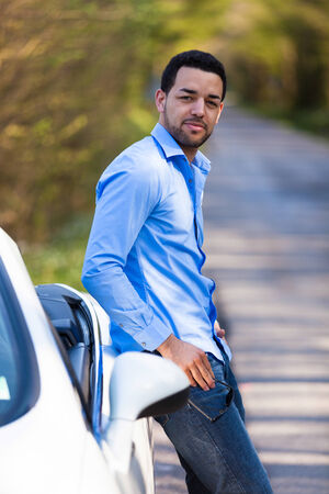 Young latin american driver seated on the side of his new carの写真素材
