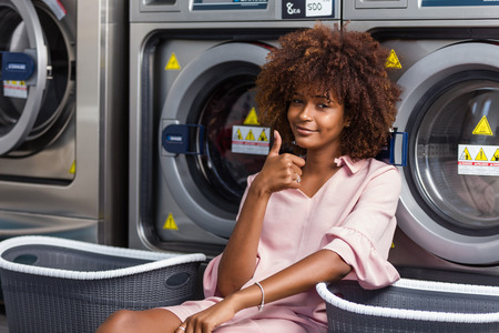 Young black African American woman waiting her clothes to be washed in a automatic laundryの写真素材