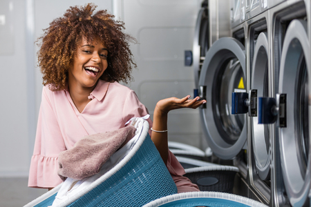 Young black African American woman holding a basket of clothes to be washed in a automatic laundryの写真素材