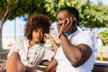 Outdoor protrait of black african american couple -  Girl bored watcing boyfriend on phoneの写真素材