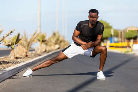 Black african american young man stretching after outdoor joggingの写真素材
