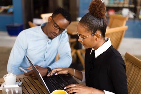 Black African American coworkers doing digital teamwork around a coffee cupの写真素材