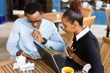 Black African American coworkers doing digital teamwork around a coffee cupの写真素材