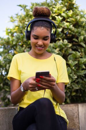 Pretty young black african american woman listening to music with a headphone outdoor