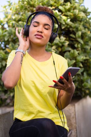 Pretty young black african american woman listening to music with a headphone outdoorの写真素材