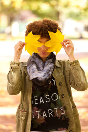 Autumn outdoor portrait of beautiful African American young woman holding yellow leaves - Black peopleの写真素材