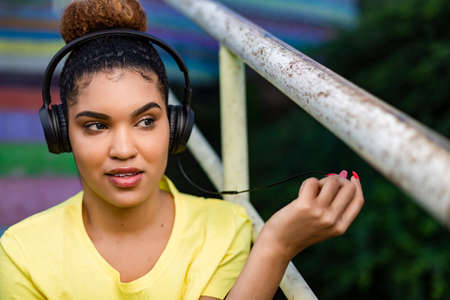 Pretty young black african american woman listening to music with a headphone outdoorの写真素材