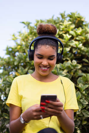 Pretty young black african american woman listening to music with a headphone outdoorの写真素材