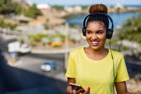 Pretty young black african american woman listening to music with a headphone outdoorの写真素材
