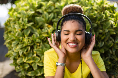 Pretty young black african american woman listening to music with a headphone outdoorの写真素材
