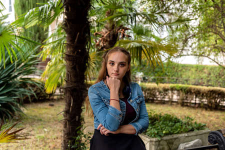 A beautiful young girl is resting and sitting on a bench in a city park.