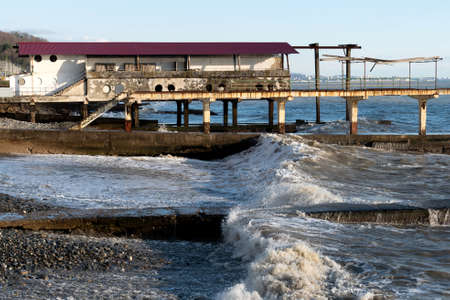 A pier on the coast against the backdrop of a raging sea in sunny weather.
