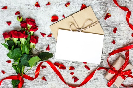 blank white greeting card and envelope with red roses flowers and red ribbon with gift boxes over rustic table. mock up. valentines day backgroundの写真素材