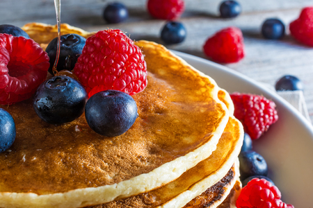 close up of homemade pancakes with fresh berries and honey on rustic wooden background for breakfast