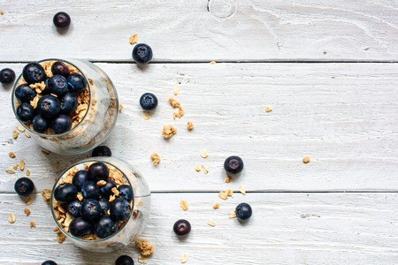 delicious blueberry yogurt dessert with granola and oats in glasses for healthy breakfast on white wooden background. top viewの写真素材