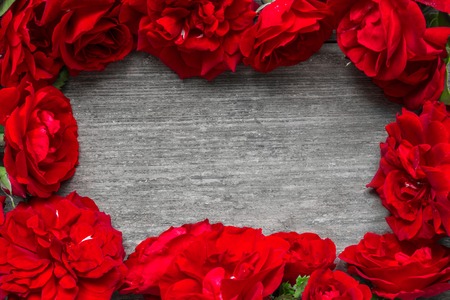 frame made of red roses flowers on rustic wooden table. valentines day or womens day background. flat lay. top view with copy spaceの写真素材
