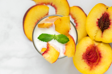 glass of healthy fruit yogurt with fresh peaches and mint on white marble table. healthy breakfast. top viewの写真素材