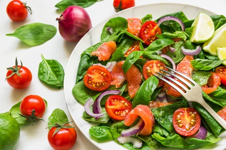 healthy food. fresh salad with salmon, spinach, cherry tomatoes, red onion and basil in marble plate with fork on white marble table. close upの写真素材