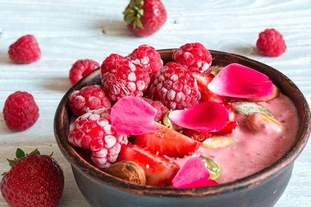 bowl of red berry smoothie with strawberry, raspberry, nuts and seeds decorated with rose flower...