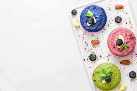 assortment of raw vegan cheesecakes with matcha, acai, butterfly pea tea, fresh berries, mint and nuts. healthy vegan food concept. top view. flat layの写真素材