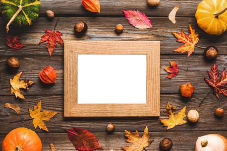 Blank photo frame with thanksgiving autumn composition. Frame made of pumpkins, fall leaves, flowers and nuts on rustic wooden table. Flat lay, top viewの写真素材