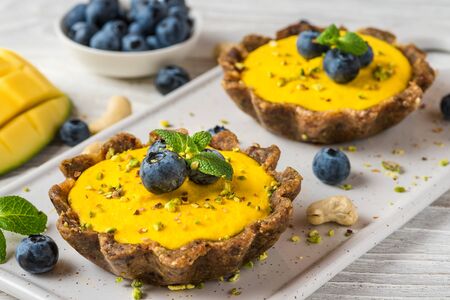 Vegan raw mango cheesecakes with fresh berries, mint and nuts. healthy vegan gluten free food concept. close upの写真素材
