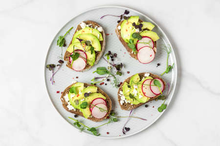 Healthy spring avocado toasts with radish, cottage cheese, pea sprouts and pepper in a plate on...