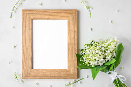 blank photo frame with lily of the valley flowers bouquet on white background. mock up. flat lay....