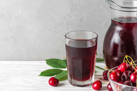 Glass of cold cherry juice with a jug and fresh berries on white background with copy space....