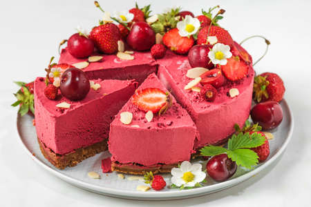 Berry cheesecake with fresh strawberries, cherries and flowers sliced in a plate on white...