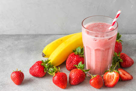 Glass of healthy smoothie or milkshake made of strawberry, banana and almond milk with a straw. Raw, vegan, vegetarian drink conceptの写真素材