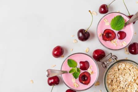 Cherry yogurt with fresh berries, oats and mint in glasses with spoons on white background. Healthy diet breakfast. top view with copy spaceの写真素材