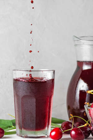 Cherry juice in a glass with drops and splash of juice and fresh berries on white background....