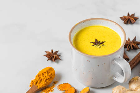 Traditional Indian drink turmeric latte or golden milk with cinnamon, ginger, anise, pepper on white background. healthy autumn or winter drink. close upの写真素材