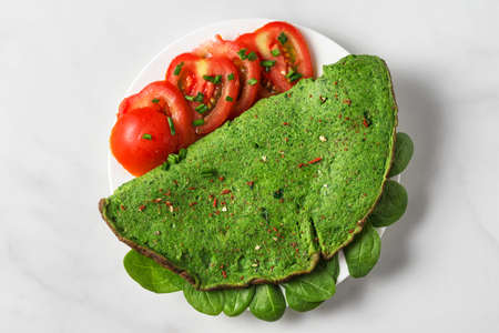 Green spinach omelette with tomatoes, spices and herbs on white marble background. Keto diet food. top viewの写真素材