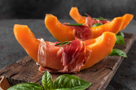 Fresh melon cantaloupe with prosciutto ham and basil on black background. Italian food appetizer. close upの写真素材
