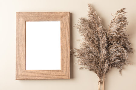 Blank photo frame with dry cane reeds or pampas grass on beige background. Flat lay. Mock up. Autumn background. Top viewの写真素材