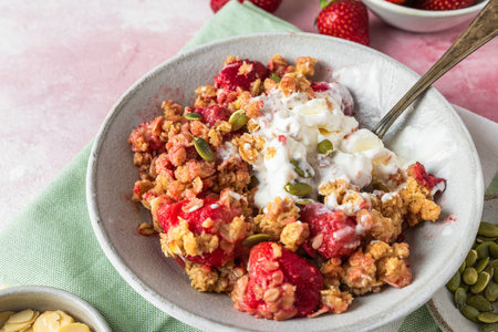 Strawberry crumble with ice cream and almonds in a plate with spoon on green napkin over pink background. tasty breakfast. Delicious foodの写真素材