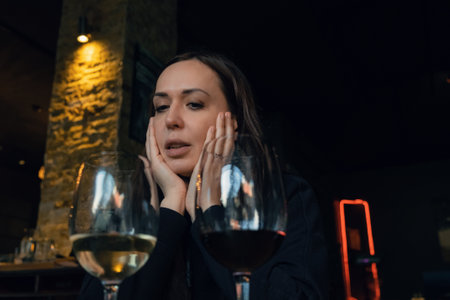 Attractive Caucasian woman looking on glasses of red and white wine in restaurant in the evening....